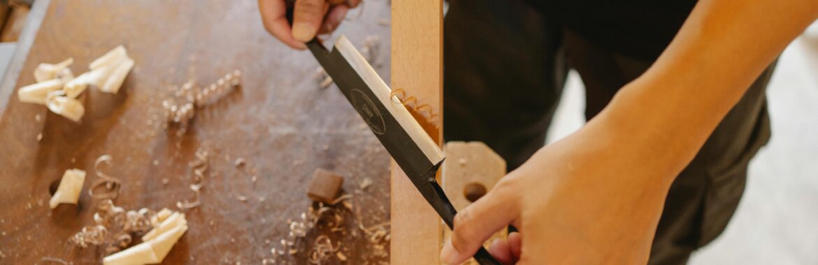 A skilled carpenter working on a wooden plank using a tool in a workshop setting.