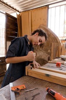 A skilled female carpenter using tools in a sunlit workshop, wearing coveralls and crafting a wooden piece.